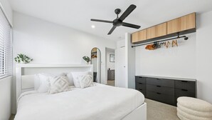A modern bedroom with a large bed, a ceiling fan, a built-in wardrobe, and a small seating area. - Spacious 1-bed Apartment in Coolangatta (Gold Coast)