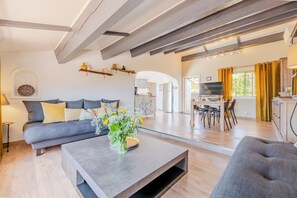 A modern living room with a sofa, coffee table, and a TV. There is a kitchen area visible in the background. - SUPERB "TOP OF VILLA" APARTMENT, PANORAMIC SEA VIEW, SWIMMING POOL (Le Lavandou)