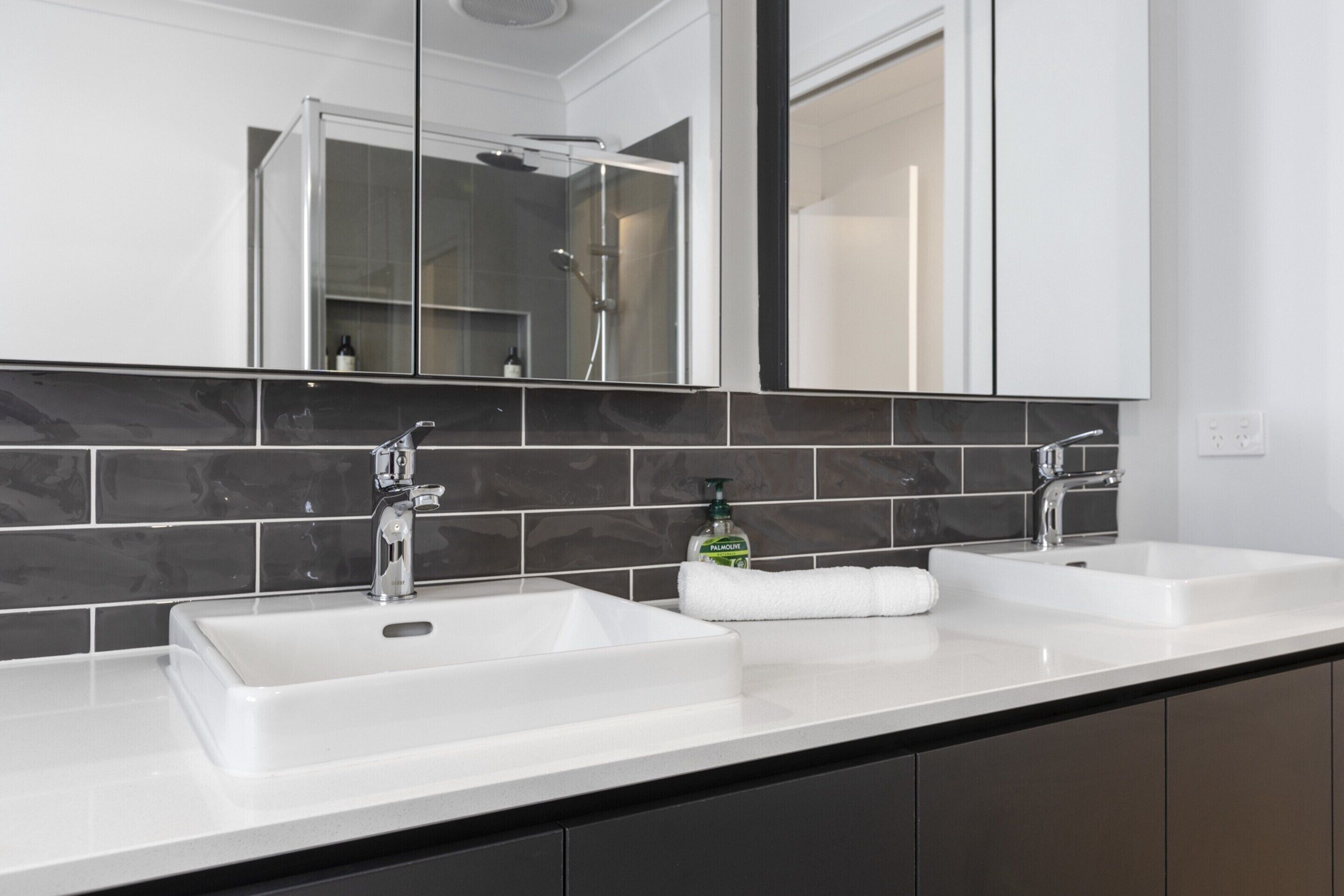 A modern bathroom with two sinks, a large mirror, and a shower.