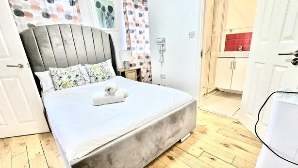 Un dormitorio con cama, una mesita de noche, un teléfono en la pared y una puerta que da a un baño.