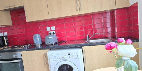 A kitchen with red tiles, a washing machine, a toaster, and a sink. - Flat 7 in Camden Parkway (London)