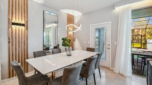 A modern dining area with a white table, grey upholstered chairs, a vase with flowers, and a pendant light. - Luxury Villa w/ Pool & Disney Themes Solterra (Davenport)
