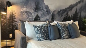 Une chambre à coucher avec un lit, des oreillers, une lampe et une fresque représentant un paysage de montagne.