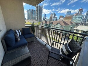 A balcony with a sofa and a chair, a railing, and a cityscape view. - Peaceful DT Condo |   Saddledome  |  HeatedParking (Calgary)