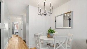 Un coin repas avec une table ronde, des chaises blanches, un lustre et une plante en pot.