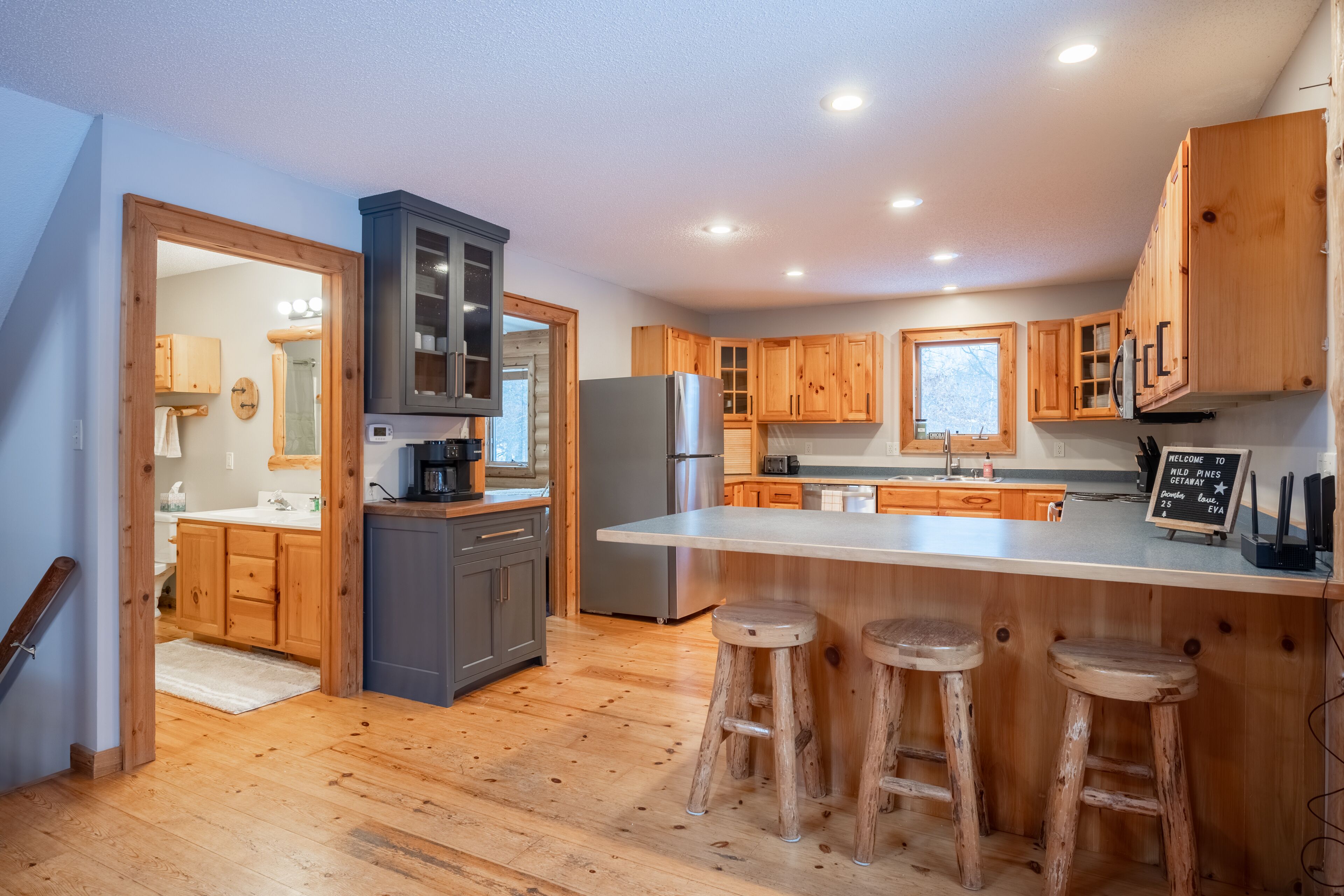 A modern kitchen with wooden cabinets, a central island with stools, and a refrigerator.