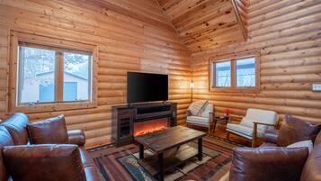 Ein rustikaler Innenraum einer Blockhütte mit Kamin, Ledersofa und Flachbildfernseher.