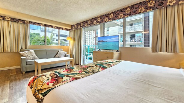 Une chambre d’hôtel avec un lit, un canapé, une télévision et un balcon donnant sur la mer.