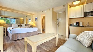 Une chambre d’hôtel comprenant un lit, un canapé, une petite table, un coin cuisine et une salle de bain, le tout visible à travers une porte ouverte.