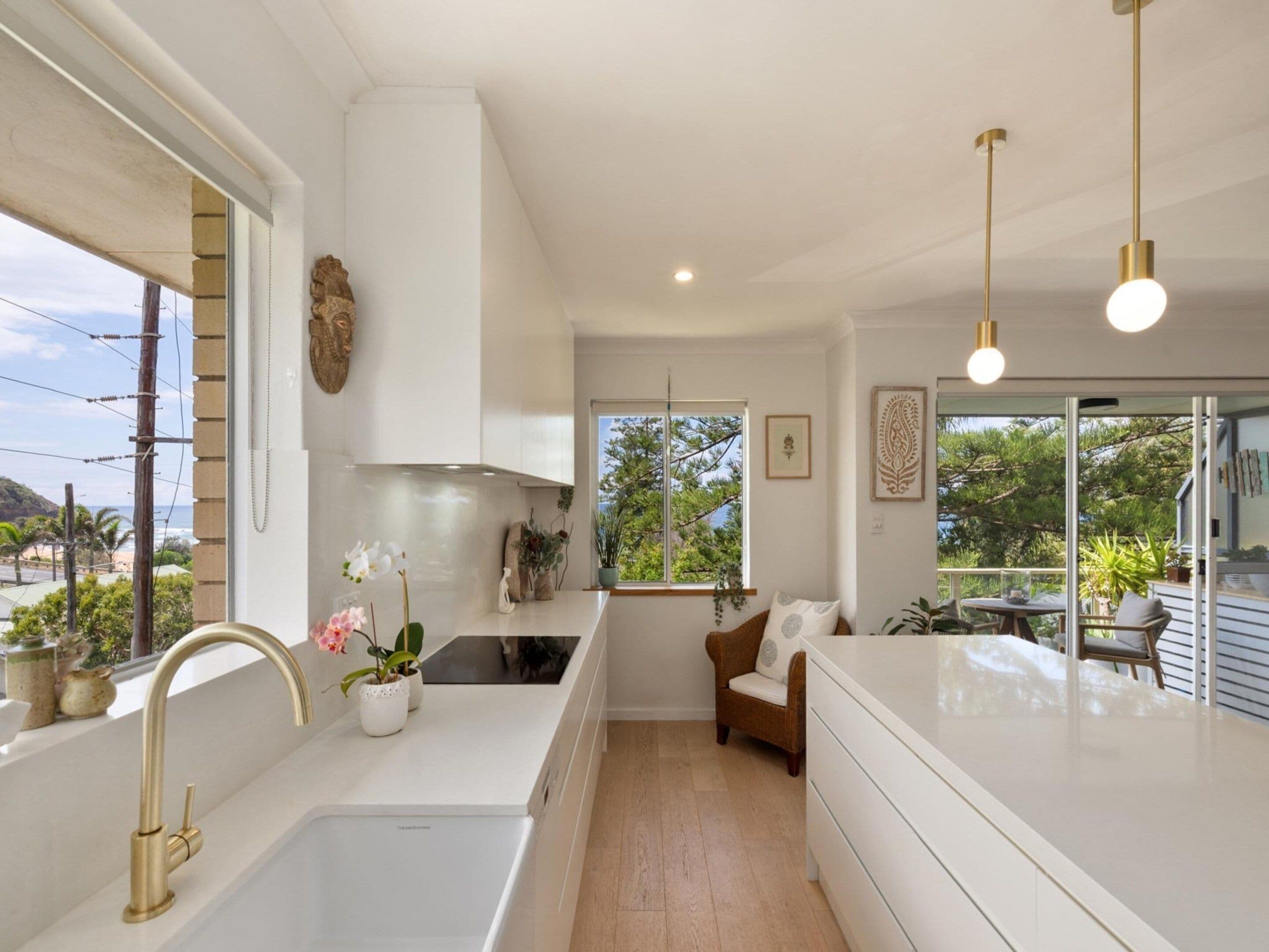 A modern kitchen with a white countertop, a gold faucet, and a view of the outdoors.