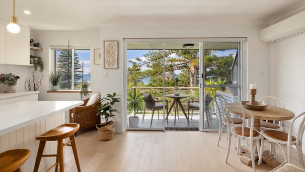 Una cocina moderna con encimera blanca, taburetes de madera y un comedor con sillas blancas y una mesa redonda.