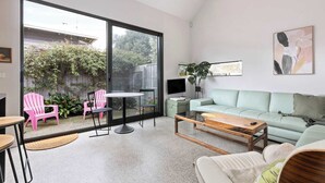 A modern living room with a large sliding glass door leading to a garden, a green sofa, a coffee table, and pink chairs. - Spacious 1-bed Townhouse in Norlane (Geelong)