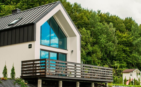 A modern two-story house with a prominent blue-tinted window, a balcony with a wooden railing, and a white exterior. - A Comfortable House in Kashubia for 4 People (gmina Stężyca)