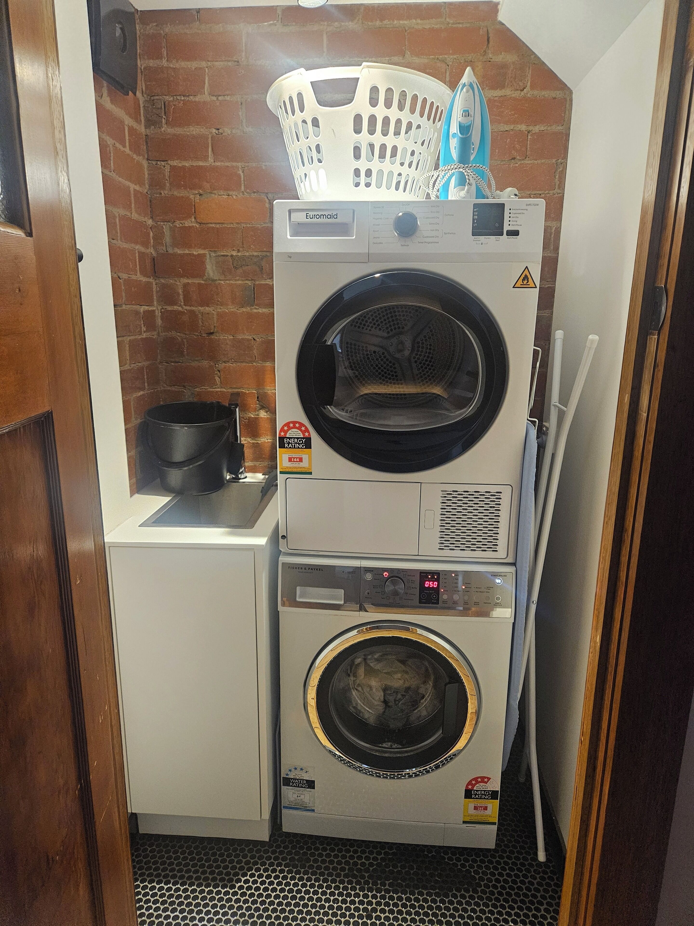 Un espace buanderie compact comprenant un lave-linge et un sèche-linge à chargement frontal, un mur en briques et un petit évier.