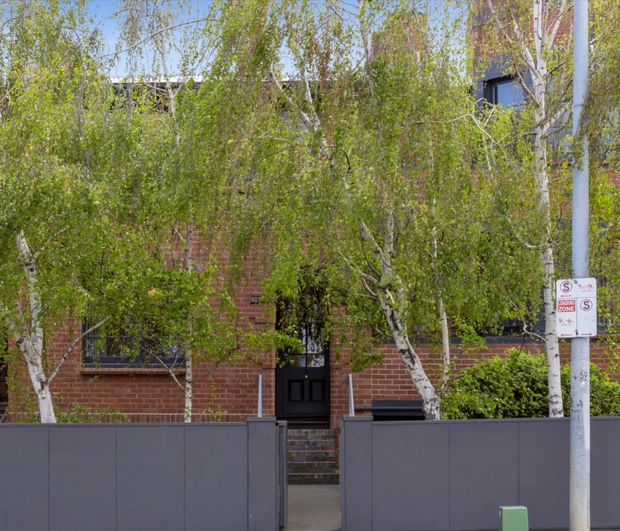 Un bâtiment en briques avec une porte noire et un portail. Un panneau indique une zone interdite d’accès.
