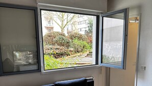 Ein Zimmer mit einem dunkelblauen Sofa, einem großen Fenster mit Blick auf einen Garten und Gebäude sowie einer Schiebetür.