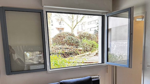 Ein dunkelblaues Sofa in einem Zimmer mit einem großen Fenster, Fliesenboden und einer Heizung.