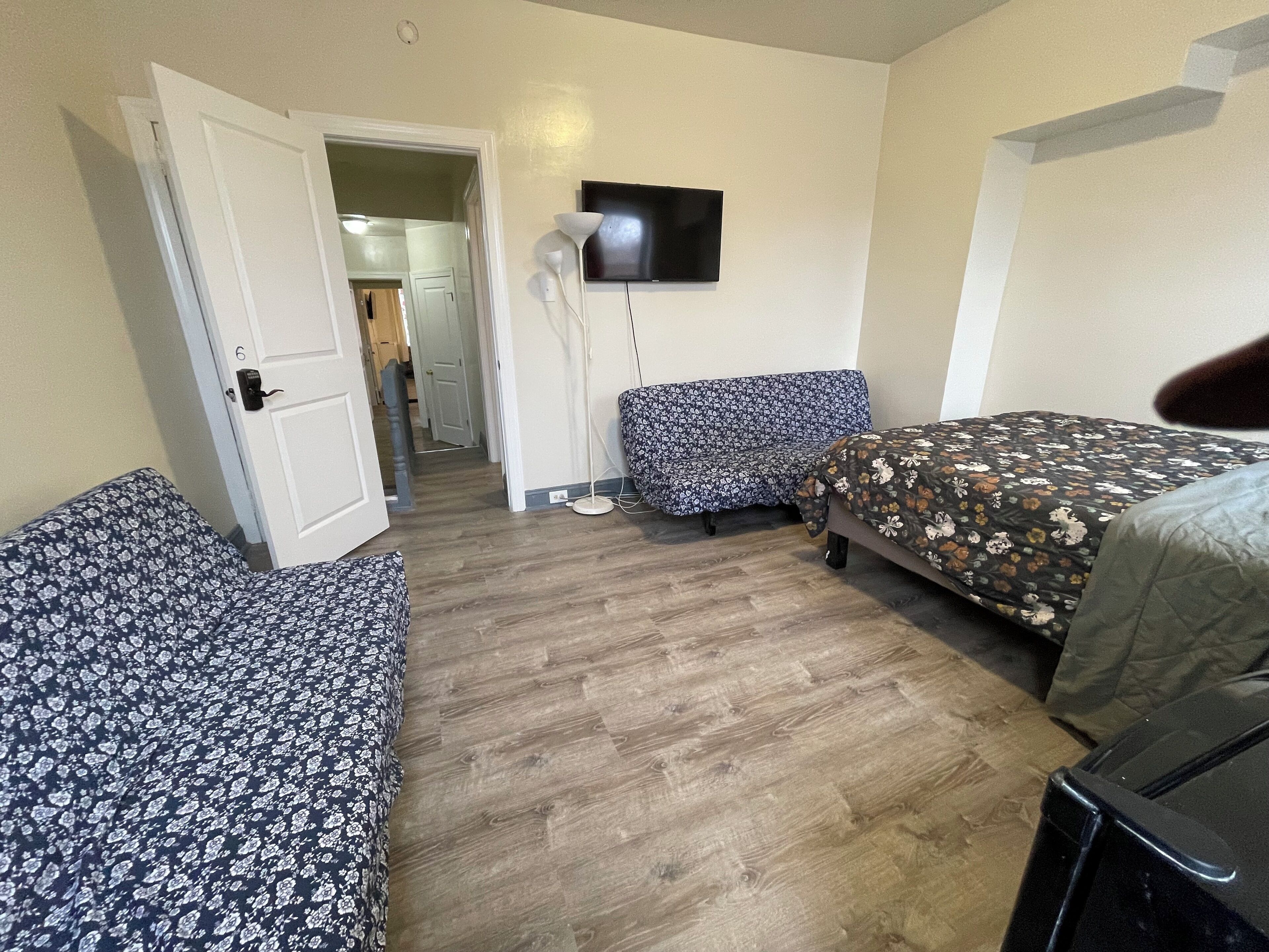 A room with a bed, a chair, a TV, and a door leading to another room.