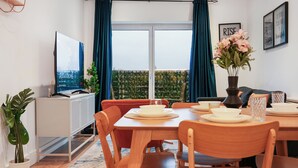 Uma área de refeições com mesa posta para quatro pessoas, uma televisão na parede e uma varanda com cortinas.