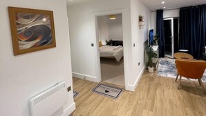 Um apartamento moderno com piso de madeira, uma cama ao fundo, um espaço de jantar com uma cadeira e um radiador na parede.