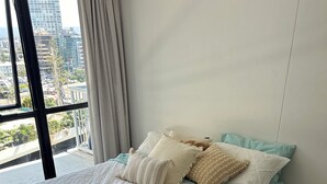 Een moderne slaapkamer met een groot bed, uitzicht op de stad door een raam en een balkon.