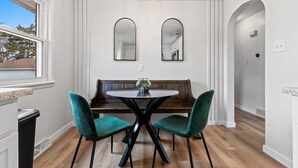 Un comedor con una mesa redonda, dos sillas verdes, un banco de madera y dos espejos de pared.