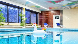 An indoor swimming pool with a swan float, chairs, and a view of trees through large windows.