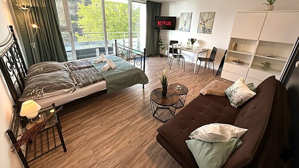 A modern hotel room with a bed, a sofa, a desk, and a TV displaying 'NETFLIX'.