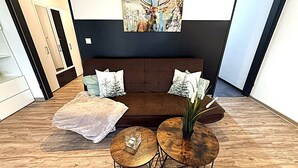 A modern living room with a brown sofa, two round wooden tables, and a painting of a deer on the wall.