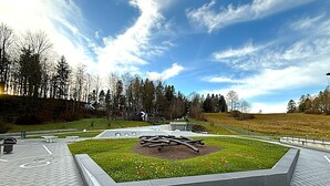 A paved area with a central grassy patch and a sculpture.