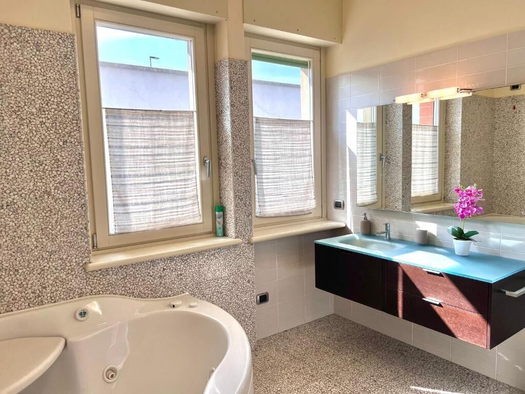 Ein modernes Badezimmer mit einer freistehenden Badewanne, zwei Fenstern mit Jalousien, einem Waschtisch und einem Spiegel.