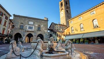 A historic square with a fountain, stone buildings, and a tall tower.