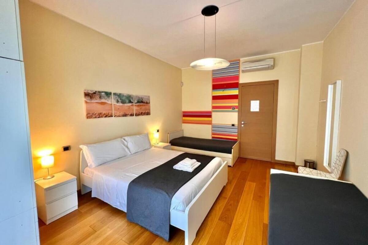 A hotel room with a bed, bedside tables, a desk, a chair, a mirror, and a colorful striped wall.