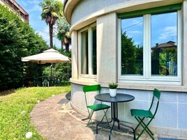 Un patio con un tavolo rotondo e due sedie, una pianta in vaso e un ombrello verde.