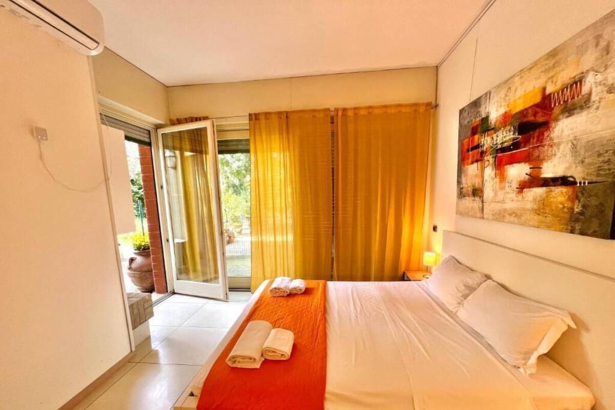 A hotel room with a bed, a red throw blanket, and a painting on the wall.