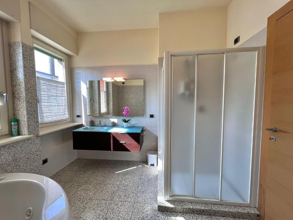 A bathroom with a white bathtub, a sink with a blue countertop, a mirror, and a frosted glass shower door.