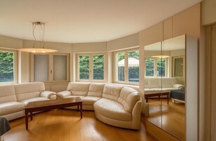 Un ampio soggiorno con un grande divano beige in pelle a forma di L, un tavolino in legno e un grande specchio che riflette l'ambiente.