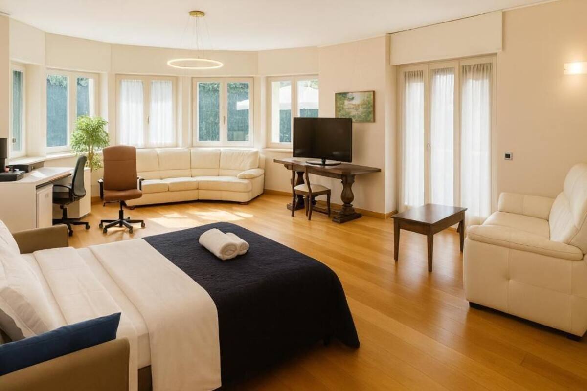 A modern hotel room with a large bed, a sofa, a desk, and a TV.
