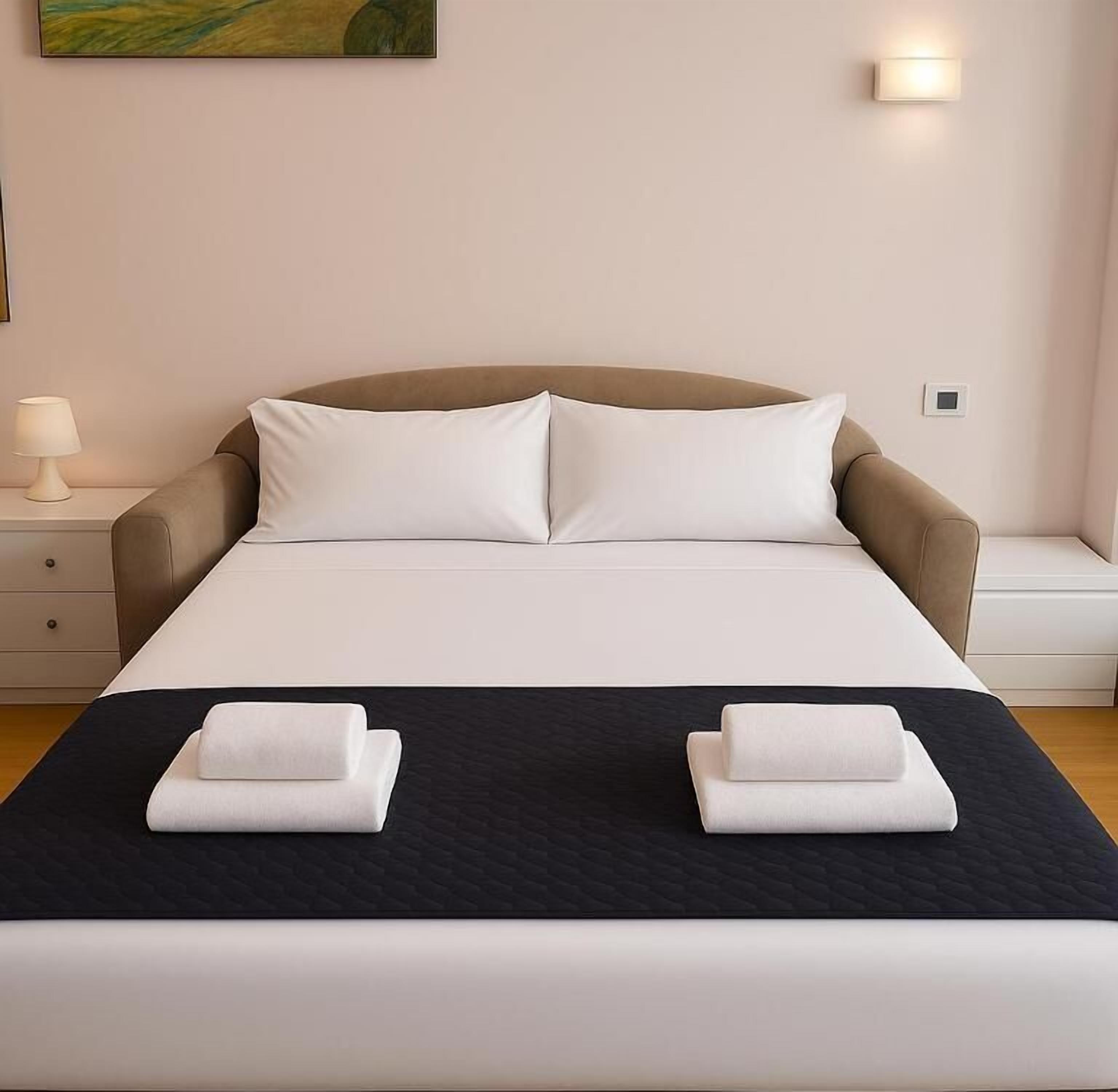 Una cama bien hecha con sábanas blancas y dos toallas dobladas sobre un edredón negro.