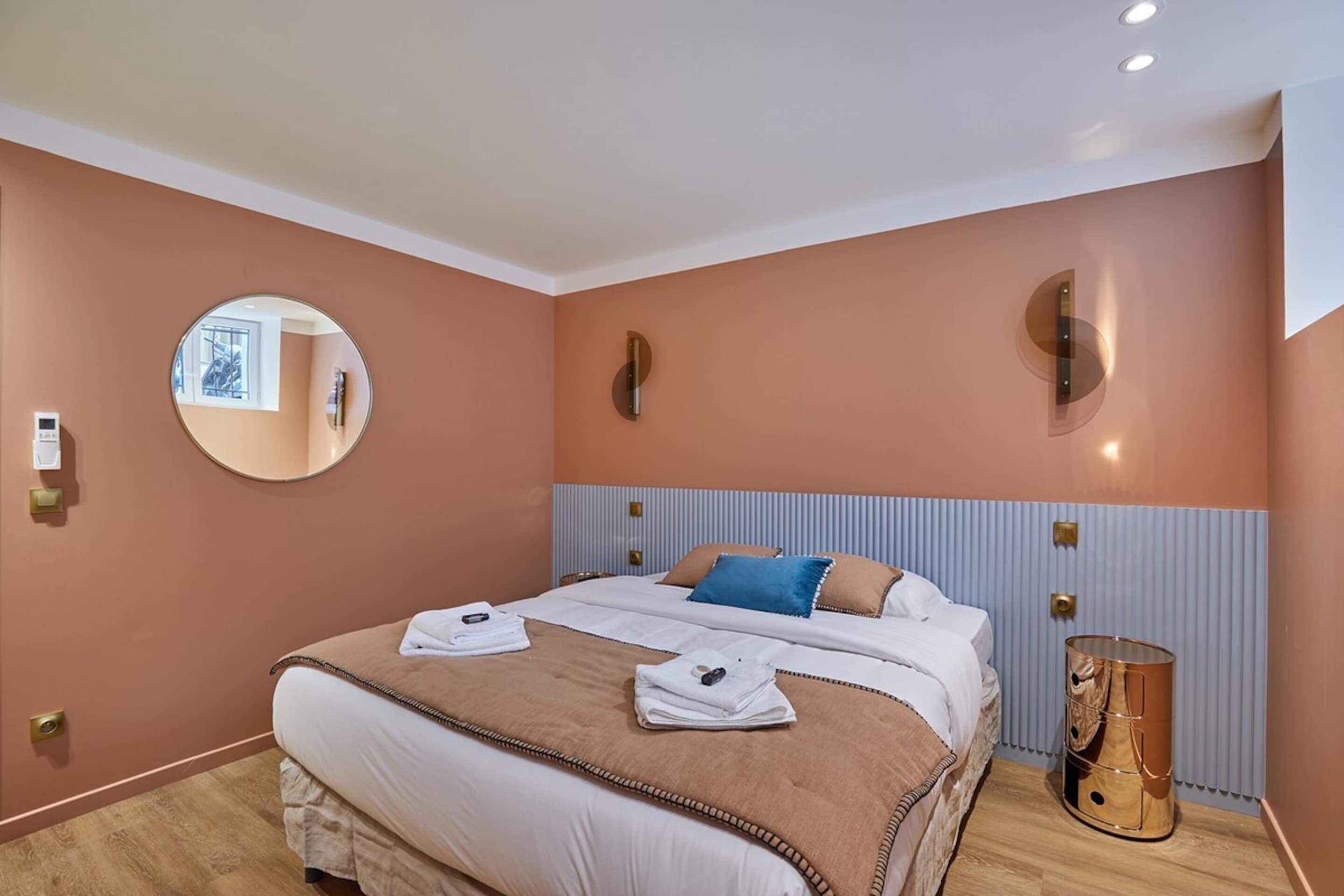 A hotel room with a large bed, a round mirror, and a unique cylindrical object on the floor.
