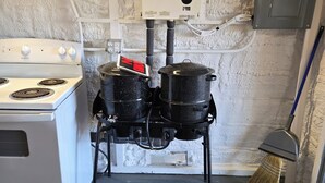 Una cocina con estufa, ollas, calentador de agua y una escoba.