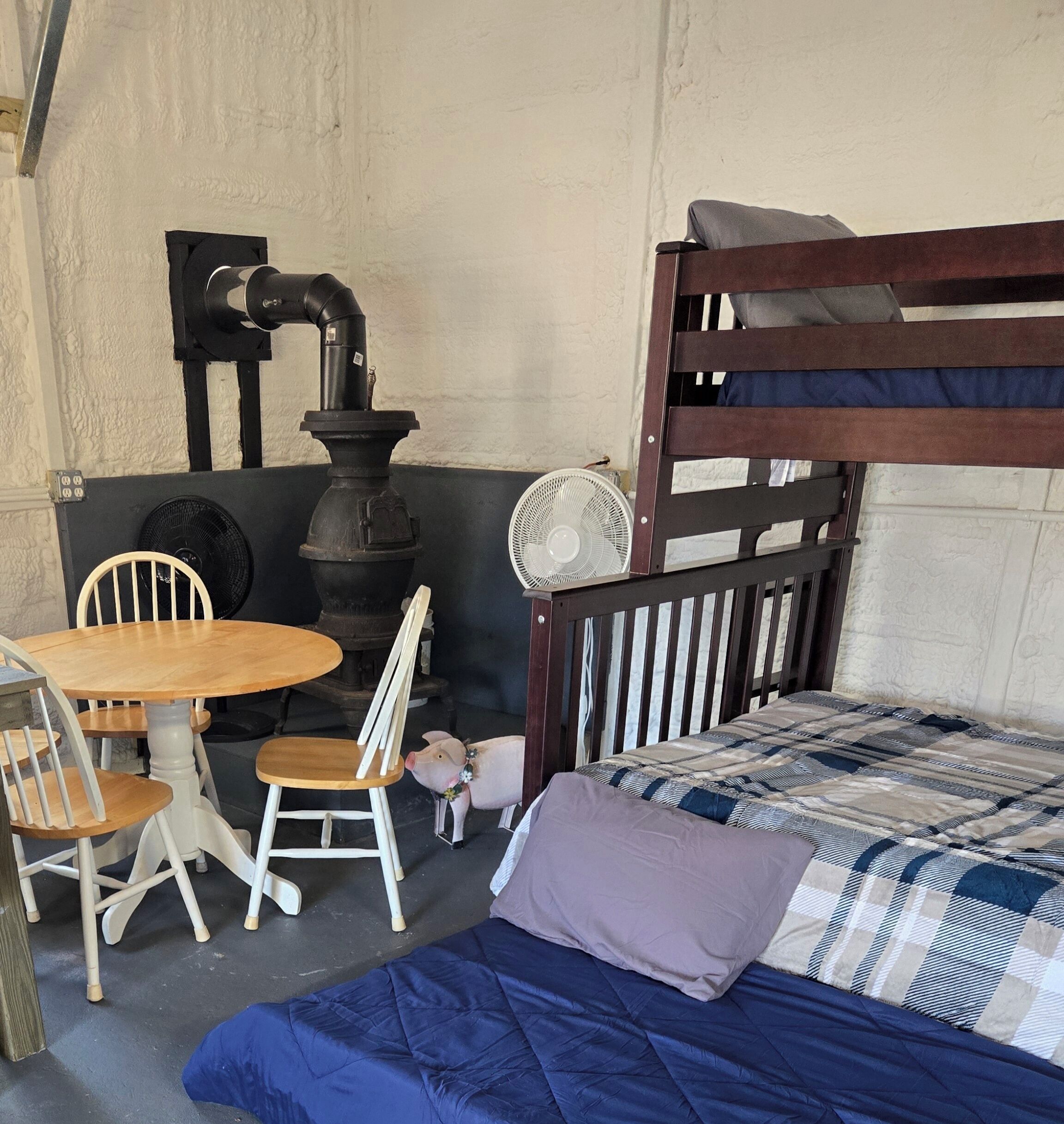 A bunk bed with a wooden headboard, a small round table with chairs, a fan, and a piggy bank on the floor.