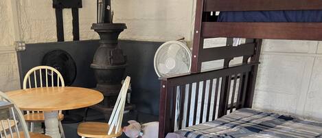 A bunk bed with a wooden headboard, a small round table with chairs, a fan, and a piggy bank on the floor.
