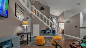 A spacious living area with a staircase, a television, a console table, and a dining area. - Family 4BR Disney-Themed Home, Screened Pool, Game Room (Kissimmee)