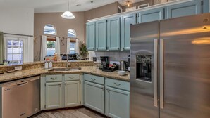 A kitchen with light blue cabinets, a stainless steel refrigerator, and a granite countertop. - Family 4BR Disney-Themed Home, Screened Pool, Game Room (Kissimmee)