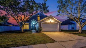 A two-story house with a garage, a front porch, and a driveway. - Family 4BR Disney-Themed Home, Screened Pool, Game Room (Kissimmee)