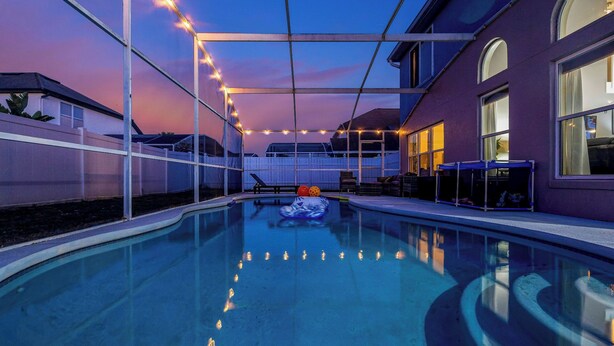 A swimming pool with a slide, surrounded by a covered area with string lights. - Family 4BR Disney-Themed Home, Screened Pool, Game Room (Kissimmee)