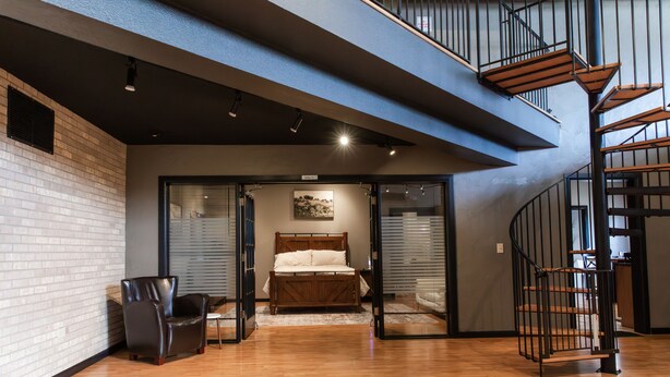 Een ruime kamer met houten vloer, een bed, een stoel en een trap.