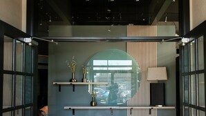 Een receptiegedeelte met een balie, planken met decoratieve objecten, een lamp en een kamerbreed tapijt met een patroon.