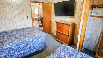 A room with two beds, a TV, a wooden dresser, and a door leading to another room.